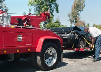 Tow truck driver securely strapping a wrecked car in preparation for towing it. Tow truck driver securely strapping a wrecked car in preparation for towing it.
